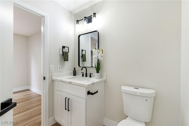 half bathroom featuring toilet, baseboards, wood finished floors, and vanity