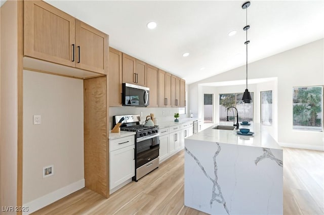 kitchen with a sink, light wood-style floors, vaulted ceiling, appliances with stainless steel finishes, and light stone countertops