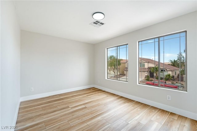 spare room with wood finished floors, visible vents, and baseboards