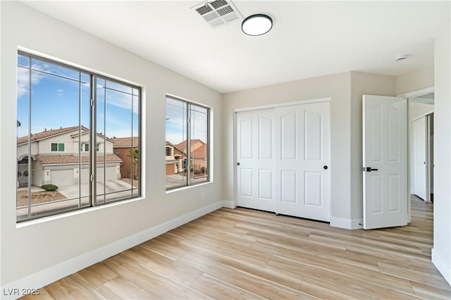 unfurnished bedroom featuring a closet, visible vents, baseboards, and wood finished floors