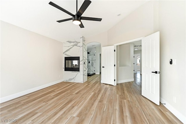 interior space featuring arched walkways, light wood-style flooring, a fireplace, a ceiling fan, and baseboards