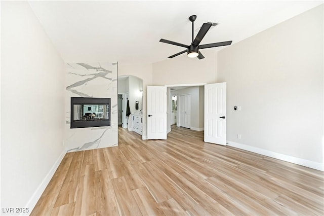 unfurnished living room featuring light wood-style flooring, arched walkways, baseboards, and a high end fireplace