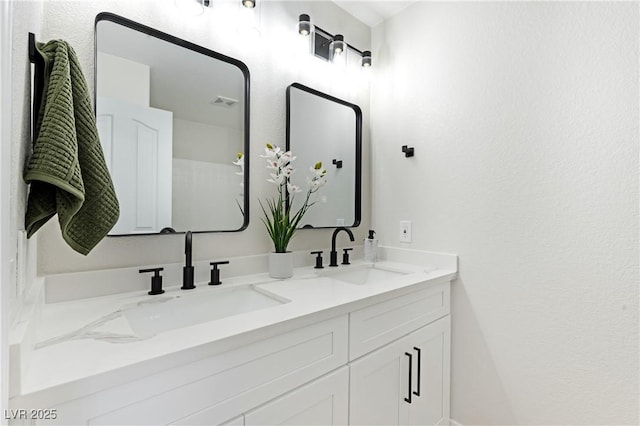 bathroom featuring a textured wall, double vanity, a sink, and visible vents