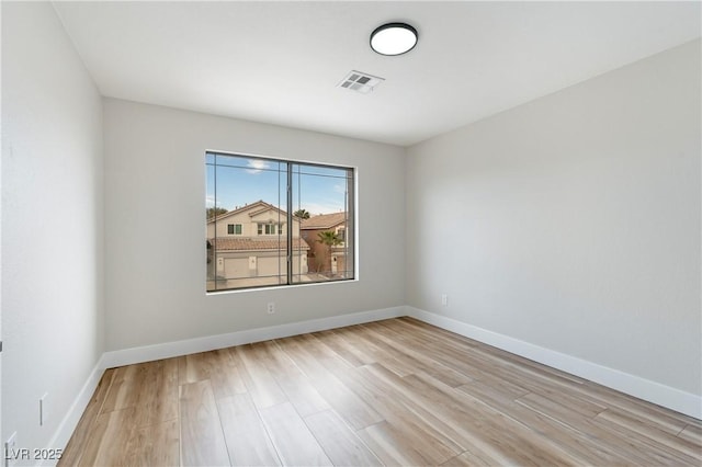 empty room featuring light wood-style flooring, visible vents, and baseboards