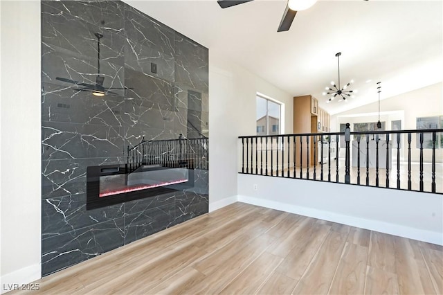 spare room featuring baseboards, lofted ceiling, wood finished floors, a fireplace, and ceiling fan with notable chandelier