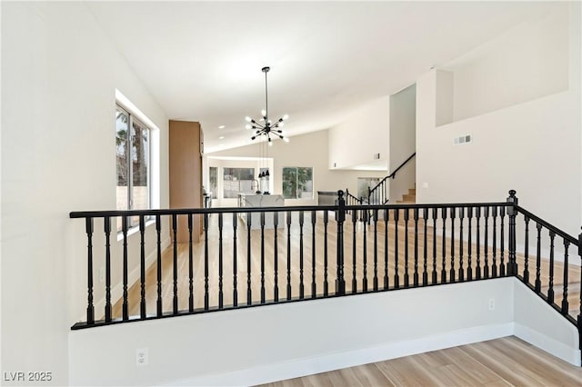 hall featuring lofted ceiling, stairs, visible vents, and a notable chandelier