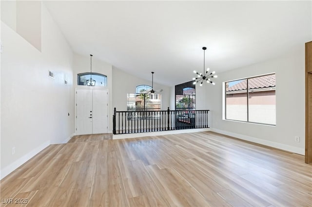 entrance foyer with light wood finished floors, baseboards, visible vents, high vaulted ceiling, and a notable chandelier