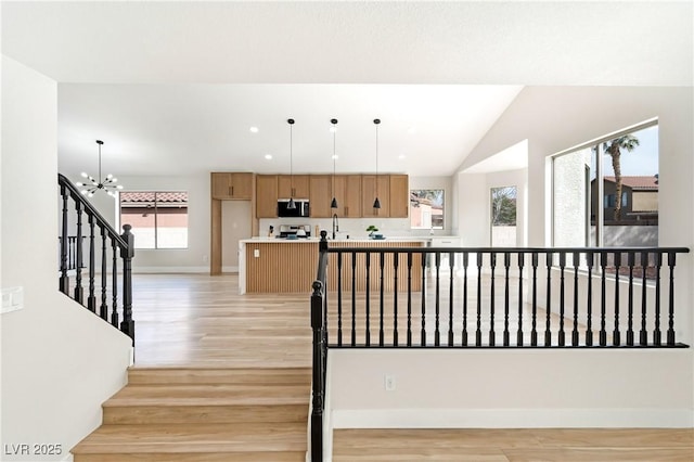 staircase featuring lofted ceiling, a notable chandelier, baseboards, and wood finished floors