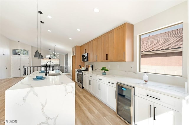 kitchen with beverage cooler, a sink, vaulted ceiling, appliances with stainless steel finishes, and plenty of natural light