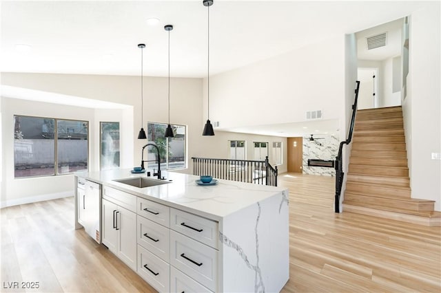 kitchen with pendant lighting, visible vents, white cabinets, a sink, and light wood-type flooring