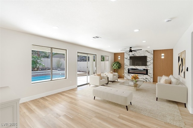 living room featuring light wood-style floors, a premium fireplace, baseboards, and a ceiling fan