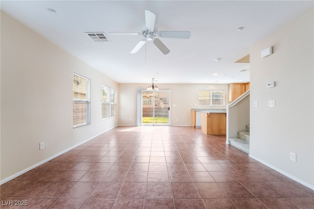 unfurnished living room with tile patterned flooring, ceiling fan with notable chandelier, visible vents, baseboards, and stairway