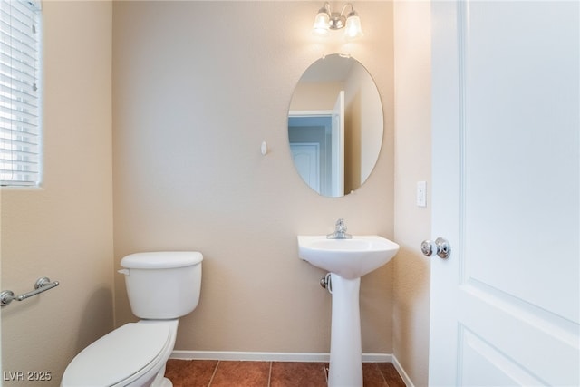 half bathroom with tile patterned flooring, baseboards, a sink, and toilet