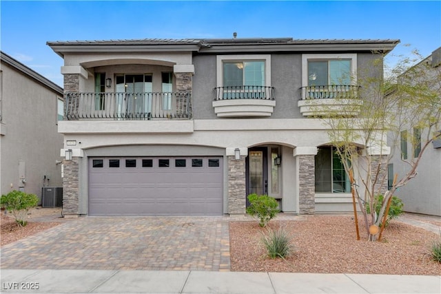 view of front of property featuring decorative driveway, stucco siding, an attached garage, a balcony, and stone siding