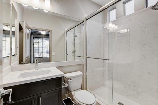 bathroom with a marble finish shower, ceiling fan, vanity, and toilet