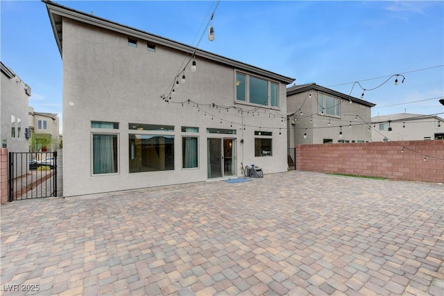 rear view of house featuring stucco siding, fence, and a patio