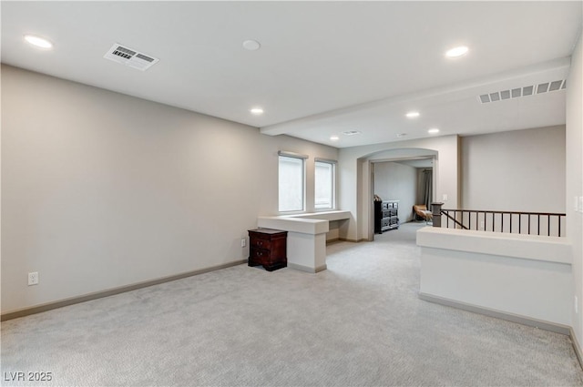 spare room featuring arched walkways, visible vents, light carpet, and baseboards