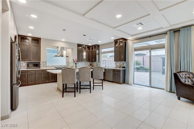 kitchen with visible vents, a breakfast bar area, stainless steel appliances, light countertops, and wall chimney range hood