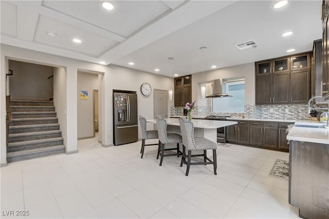 kitchen with visible vents, wall chimney exhaust hood, a kitchen breakfast bar, stainless steel appliances, and dark brown cabinets