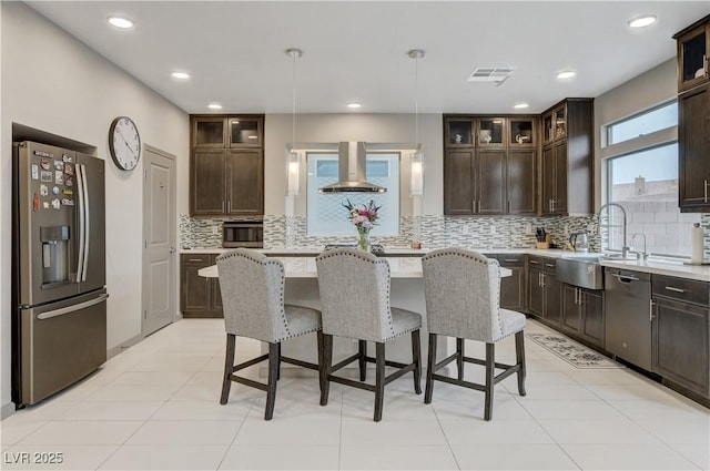 kitchen with appliances with stainless steel finishes, a breakfast bar, dark brown cabinets, wall chimney range hood, and a sink