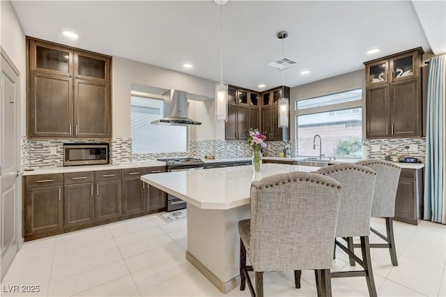 kitchen with a sink, exhaust hood, dark brown cabinets, appliances with stainless steel finishes, and a center island