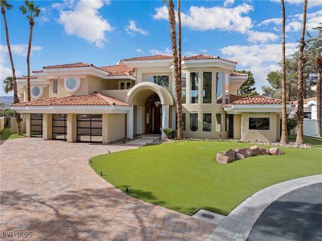 mediterranean / spanish-style home with decorative driveway, a tile roof, stucco siding, an attached garage, and a front lawn