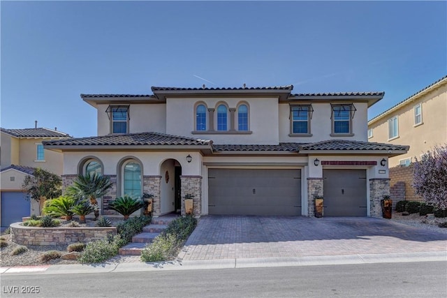 mediterranean / spanish home featuring stone siding, decorative driveway, an attached garage, and stucco siding