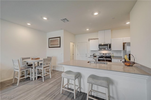 kitchen featuring a peninsula, a sink, visible vents, a kitchen breakfast bar, and appliances with stainless steel finishes