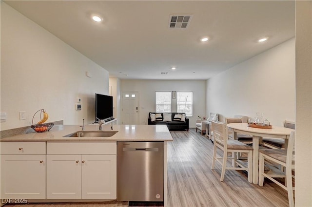 kitchen with light wood-style flooring, stainless steel dishwasher, white cabinets, a sink, and a peninsula