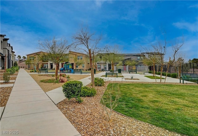 view of community featuring playground community, a lawn, fence, and a residential view