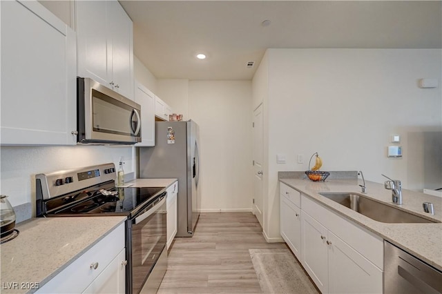 kitchen with white cabinets, light wood-style flooring, light stone counters, appliances with stainless steel finishes, and a sink