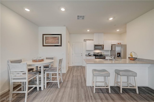 kitchen featuring visible vents, white cabinets, appliances with stainless steel finishes, a breakfast bar, and a sink