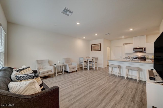 living room with light wood-type flooring, visible vents, and recessed lighting