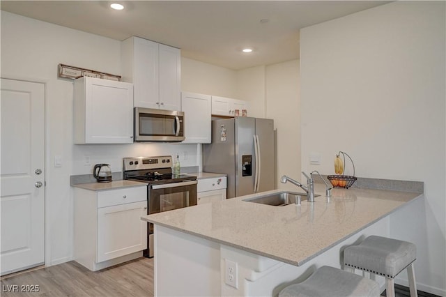 kitchen with a breakfast bar, stainless steel appliances, white cabinetry, a sink, and a peninsula