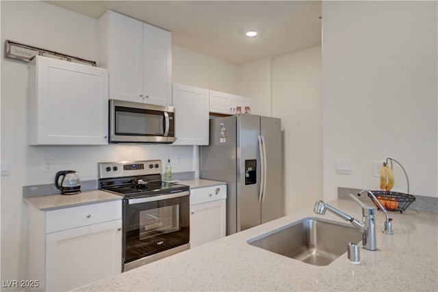 kitchen featuring appliances with stainless steel finishes, light stone counters, white cabinetry, a sink, and recessed lighting