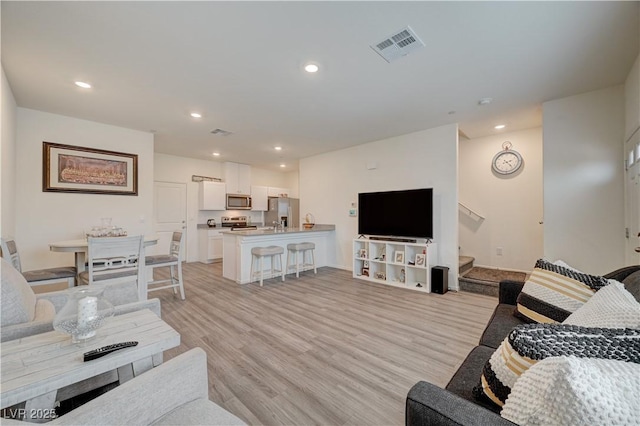 living room featuring light wood finished floors, stairs, visible vents, and recessed lighting