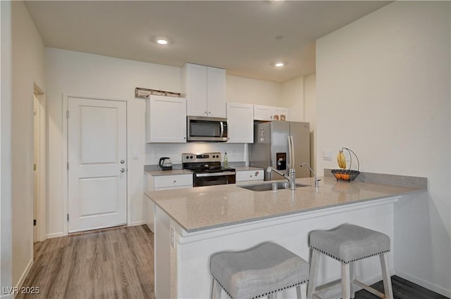 kitchen with white cabinets, appliances with stainless steel finishes, a breakfast bar, a peninsula, and a sink