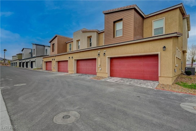 view of property featuring a garage, a residential view, cooling unit, and stucco siding