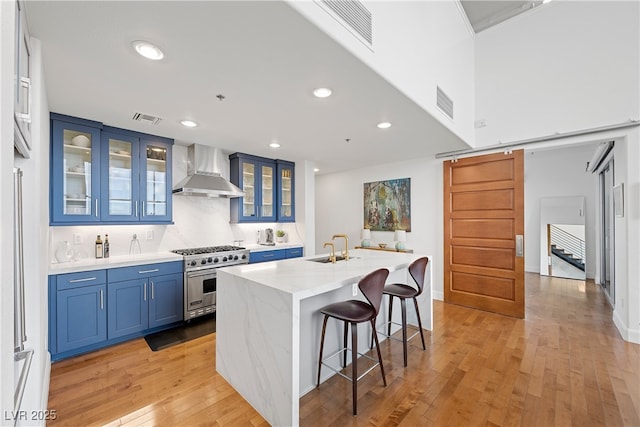 kitchen featuring a barn door, visible vents, wall chimney range hood, high end stainless steel range, and blue cabinetry