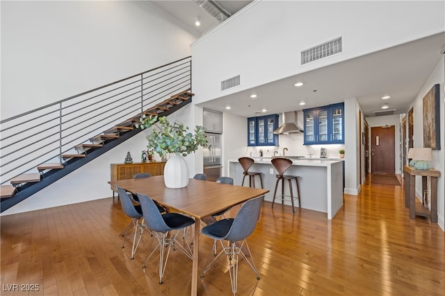 dining room featuring a high ceiling, visible vents, light wood finished floors, and stairs