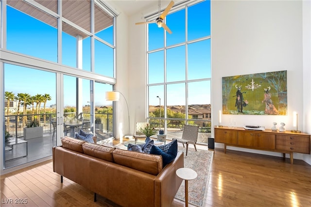 living room with a ceiling fan, a towering ceiling, and hardwood / wood-style floors