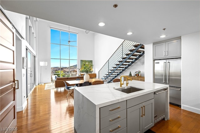 kitchen featuring light stone counters, hardwood / wood-style floors, stainless steel appliances, gray cabinets, and a sink