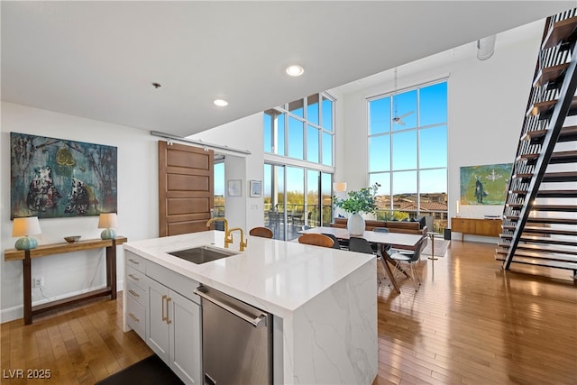 kitchen with a high ceiling, a barn door, a sink, dishwasher, and hardwood / wood-style flooring