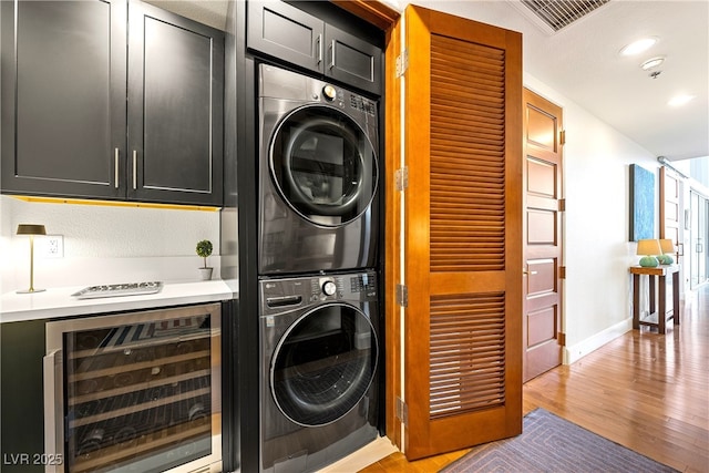 washroom featuring light wood finished floors, stacked washer / drying machine, visible vents, beverage cooler, and baseboards