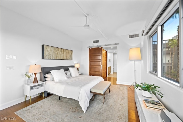 bedroom featuring baseboards, a barn door, visible vents, and hardwood / wood-style floors