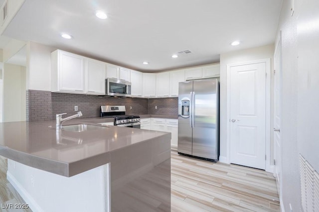 kitchen featuring tasteful backsplash, appliances with stainless steel finishes, a peninsula, white cabinetry, and a sink