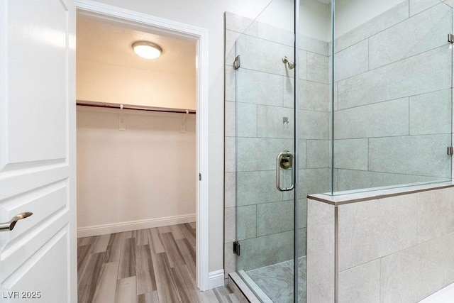 full bathroom with a walk in closet, baseboards, wood finished floors, and a shower stall