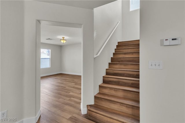 staircase with baseboards, wood finished floors, and visible vents