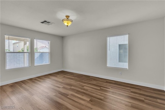 spare room featuring baseboards, wood finished floors, and visible vents