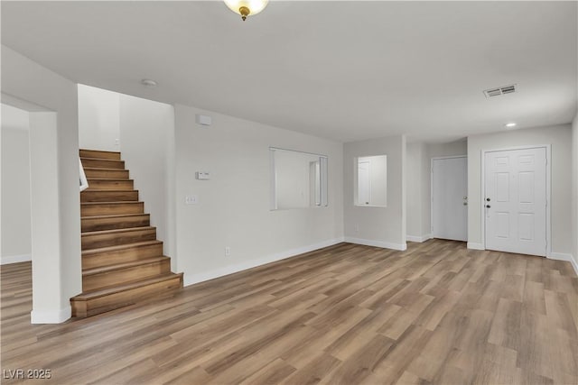 unfurnished living room with light wood-style floors, baseboards, stairs, and visible vents